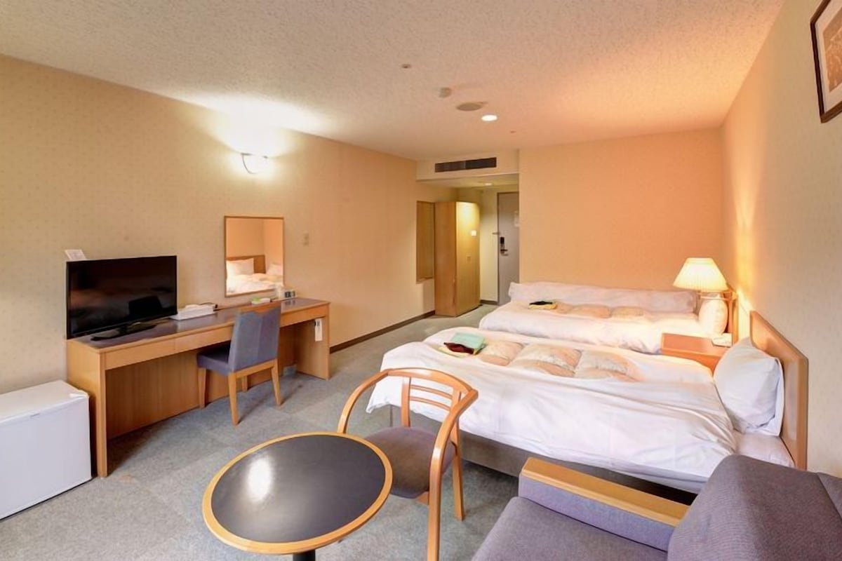 Ein Hotelzimmer mit Bett, Schreibtisch, Stuhl, Fernseher und einem kleinen Tisch.