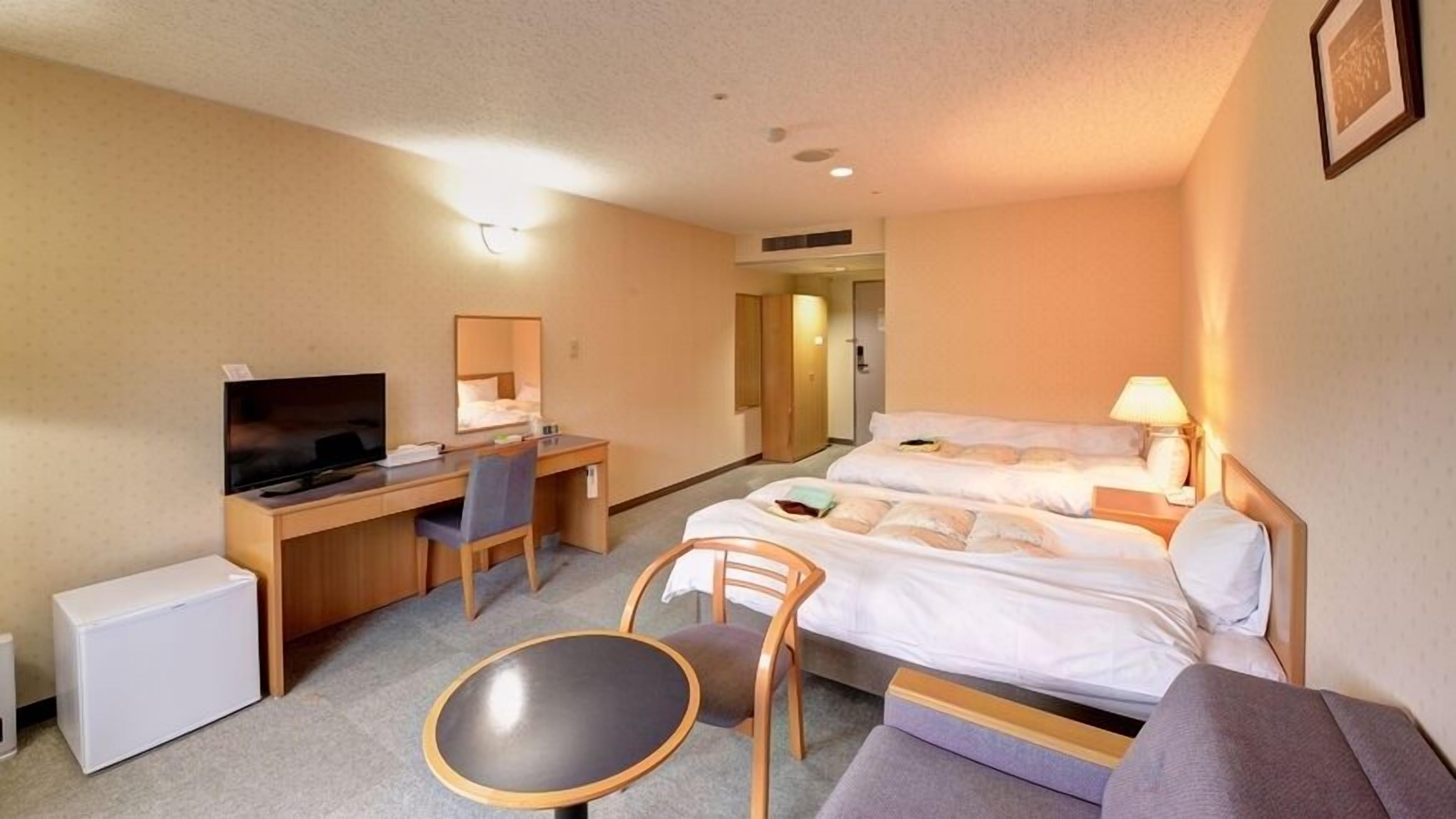 Habitación de hotel con cama, escritorio, silla, televisor y una mesita.