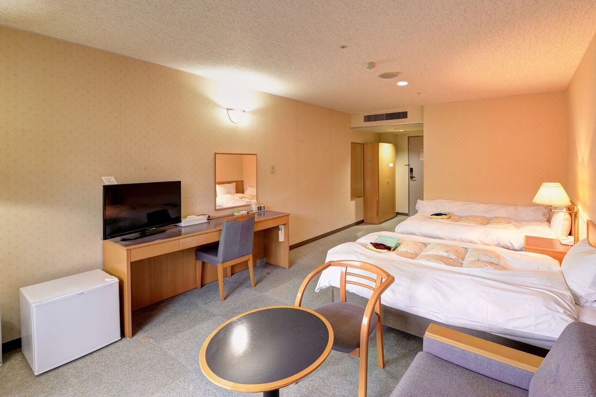 Hotellihuone, jossa on sänky, työpöytä, jossa on televisio, tuoli, pieni pöytä ja vaatekaappi.