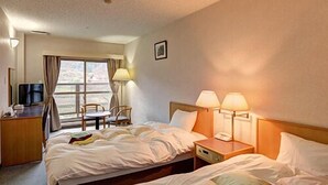 Habitación de hotel con dos camas, un escritorio con televisor y una ventana con cortinas.