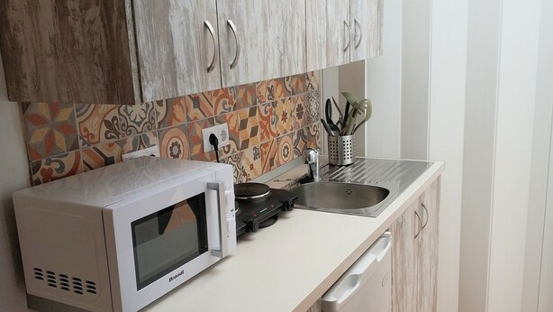 A compact kitchen with a microwave, a small sink, and a dish rack.