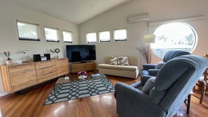 Un salon spacieux avec un meuble en bois, un téléviseur à écran plat, un canapé beige et un fauteuil gris.