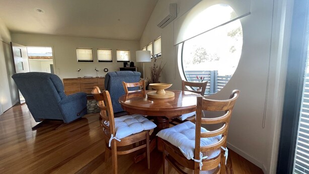 Un coin repas comprenant une table ronde en bois, six chaises en bois avec des coussins blancs et un fauteuil bleu.