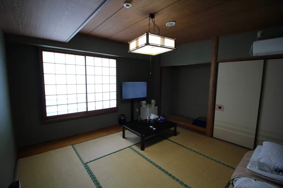 A traditional Japanese room with tatami flooring, a low table, a television, and sliding doors.