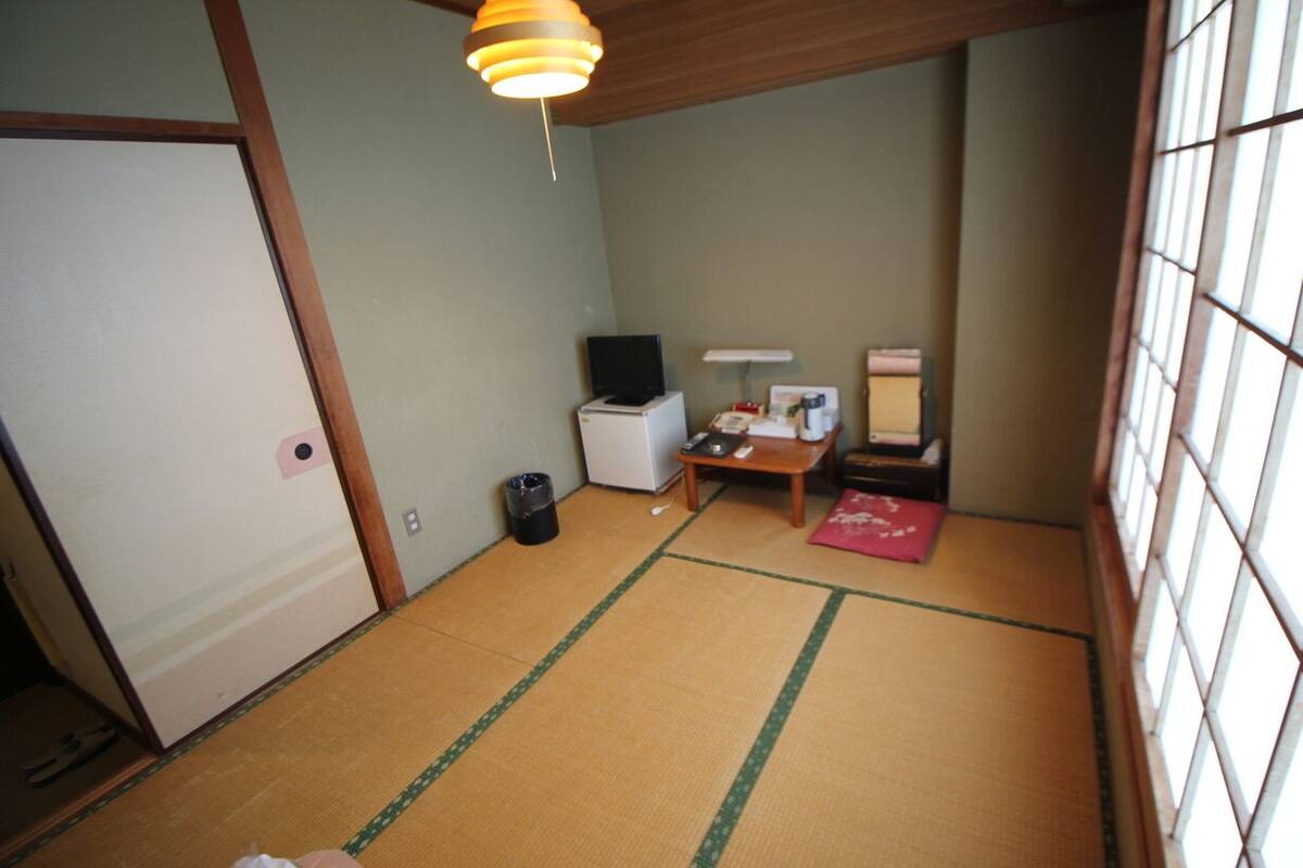 Ein Zimmer mit Tatami-Boden, einem Fernseher, einem kleinen Tisch und einem Fenster mit Blick.