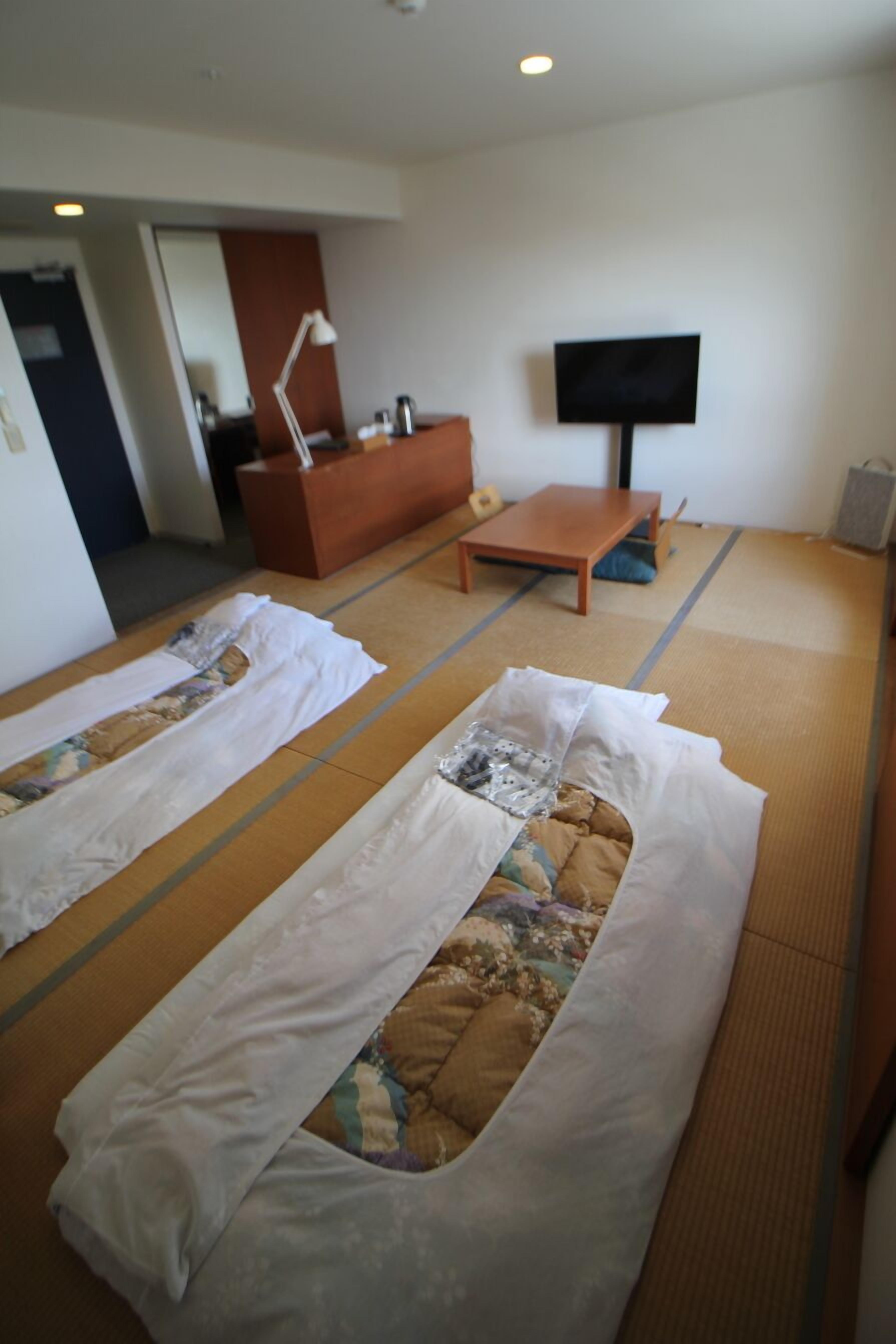 Ein Zimmer mit Tatami-Matten, einem Fernseher, einem Sofa und einem kleinen Tisch.