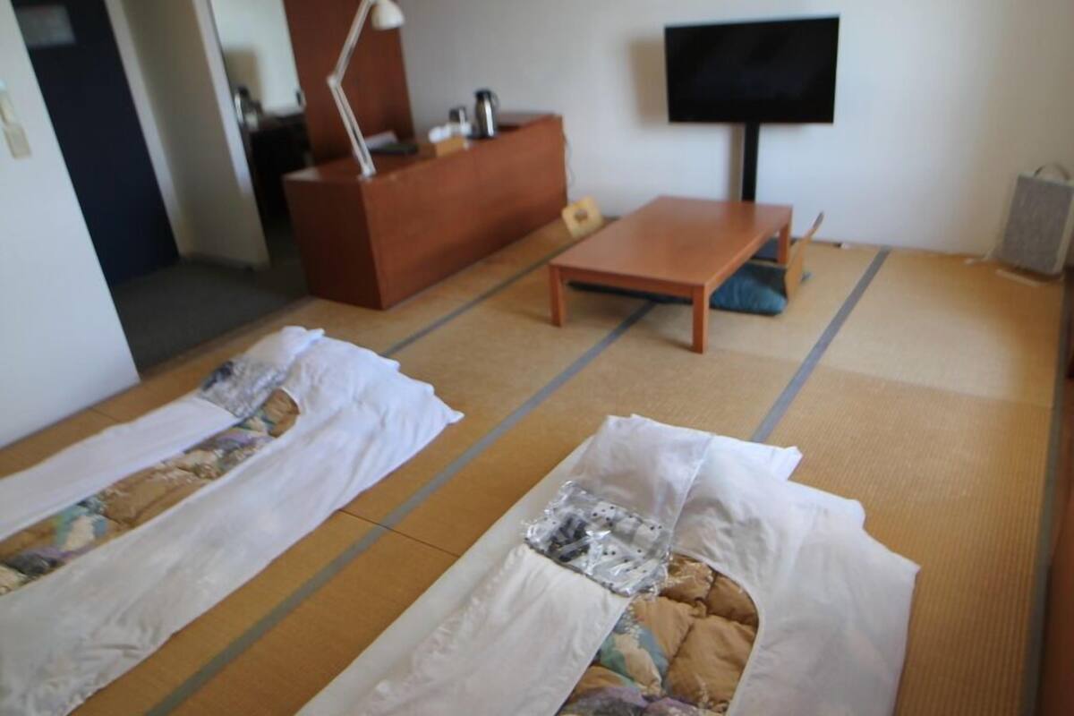 Ein Zimmer mit Tatami-Matten, einem Fernseher, einem Sofa und einem kleinen Tisch.