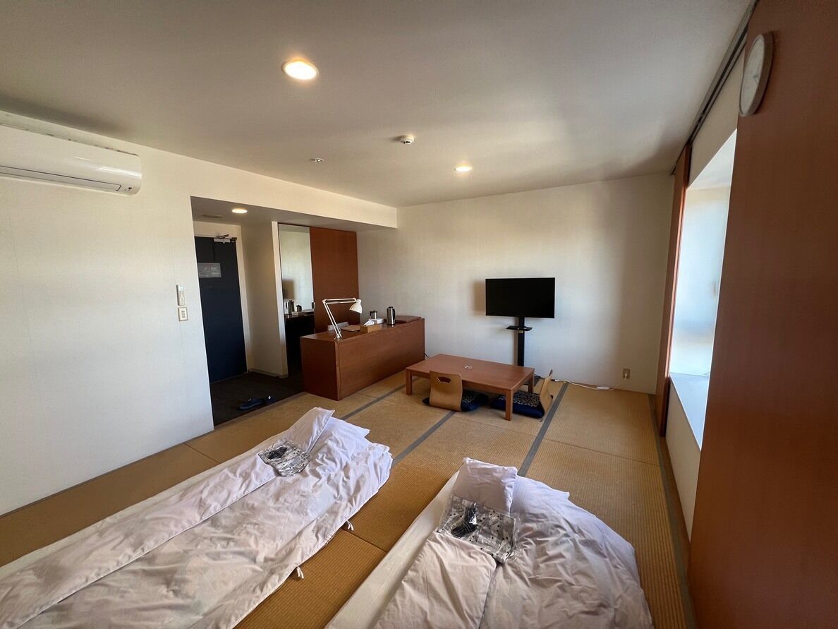 Ein Hotelzimmer mit Tatami-Matten, einer Couch, einem Fernseher und einem Holzkasten.