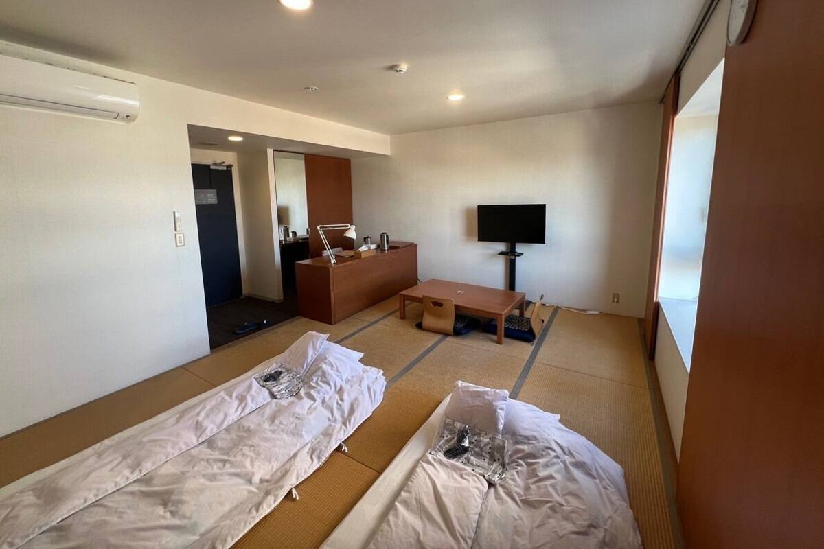 Ein Hotelzimmer mit Tatami-Matten, einer Couch, einem Fernseher und einem Holzkasten.