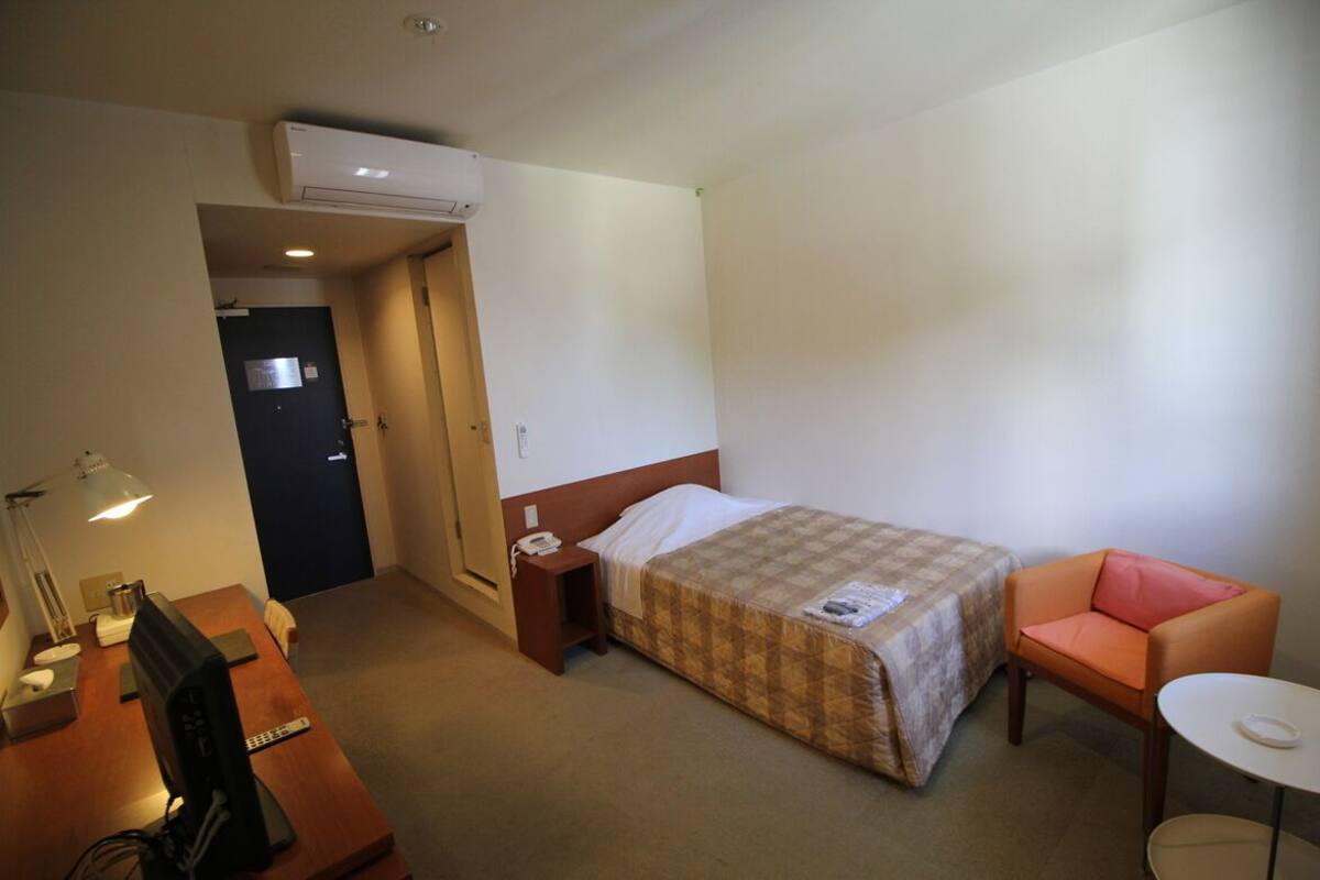 Ein Hotelzimmer mit einem Bett, einem Schreibtisch mit Computer, einem Sessel, einem kleinen Tisch und einer Klimaanlage.