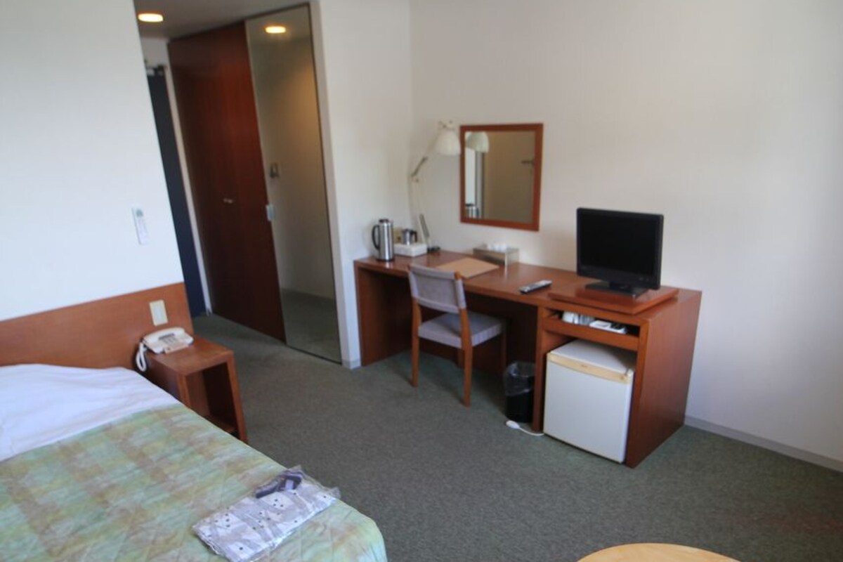Habitación de hotel con cama, escritorio, silla, refrigerador pequeño y una mesa redonda.