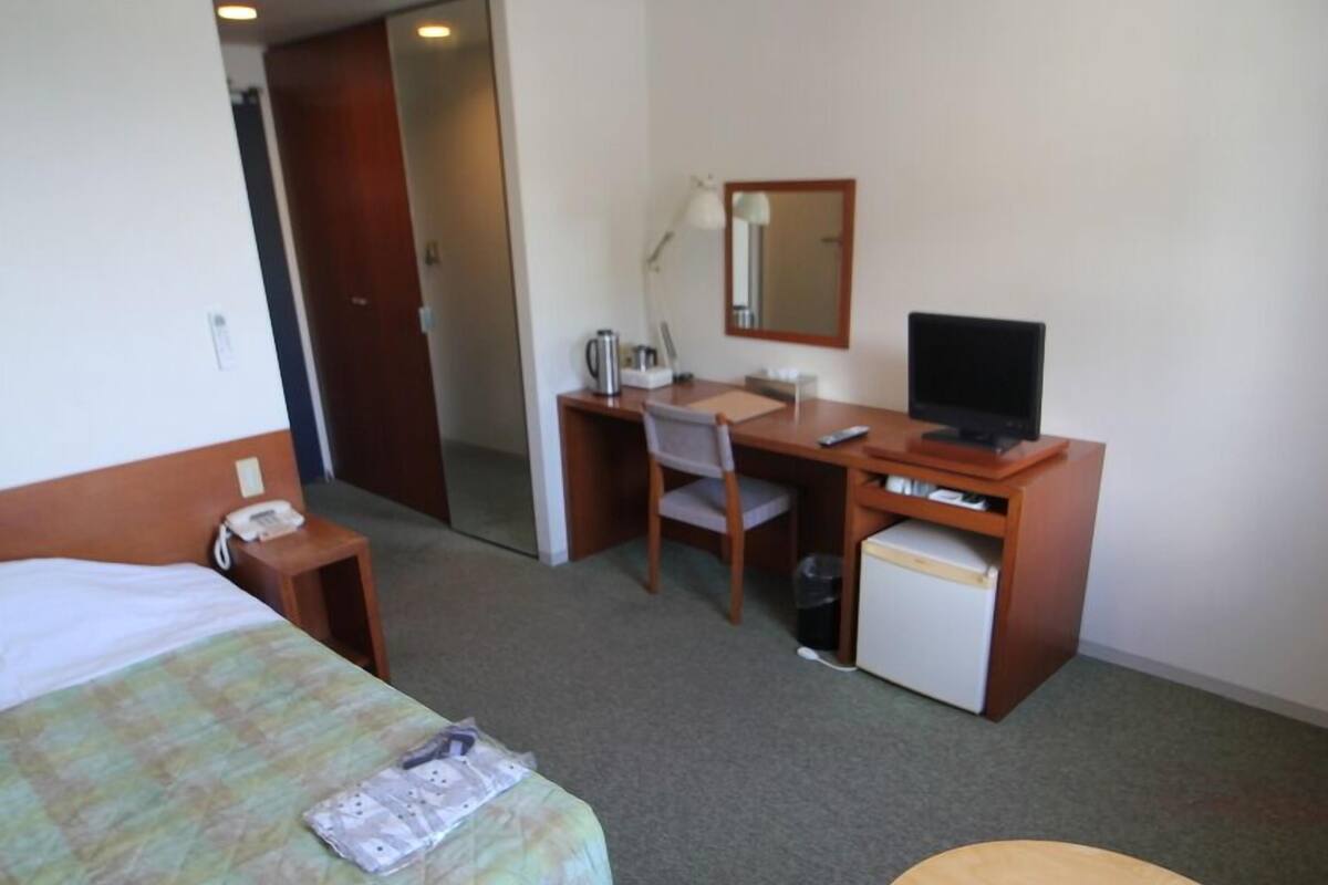 Ein Hotelzimmer mit Bett, Schreibtisch, Stuhl, kleinem Kühlschrank und einem runden Tisch.