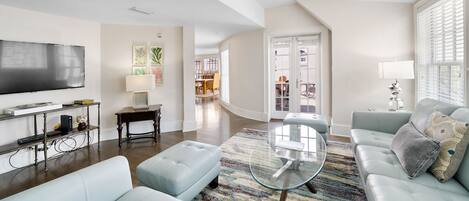 A spacious living room with a flat-screen TV, a glass coffee table, and light blue sofas.