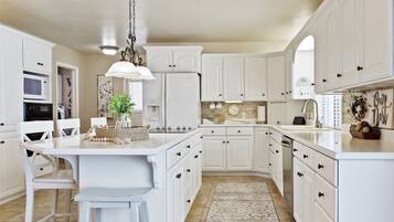 A kitchen with white cabinetry, a central island with bar stools, a hanging light fixture, and a patterned rug.