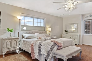 A bedroom with a bed, bedside tables, a nightstand, a chandelier, and a window.