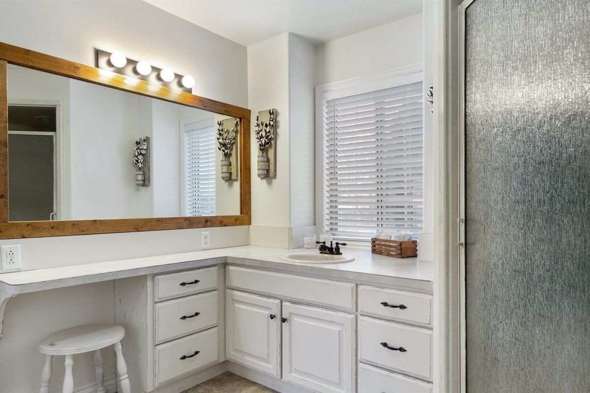 A bathroom with a white vanity, a large mirror, and a window with blinds.