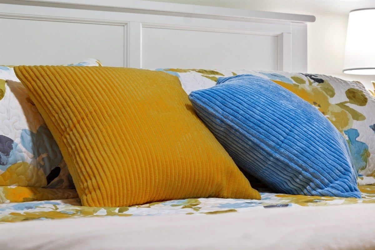 A bed with a floral-patterned bedspread and two pillows, one yellow and one blue.