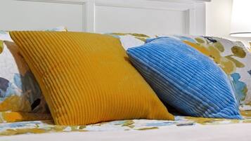 A bed with a floral-patterned bedspread and two pillows, one yellow and one blue.