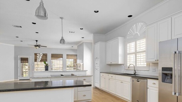 A modern kitchen with white cabinets, a black countertop, a stainless steel refrigerator, and a ceiling fan. - Stunning views of 17th hole at Austin Country Club.  (Austin)