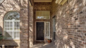 A brick building with a black door, a window with a grid pattern, and a potted plant. - Stunning views of 17th hole at Austin Country Club.  (Austin)