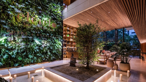 Un hall d’hôtel agrémenté d’un jardin vertical, d’un grand bac central planté d’un arbre et d’un espace détente avec des bougies.