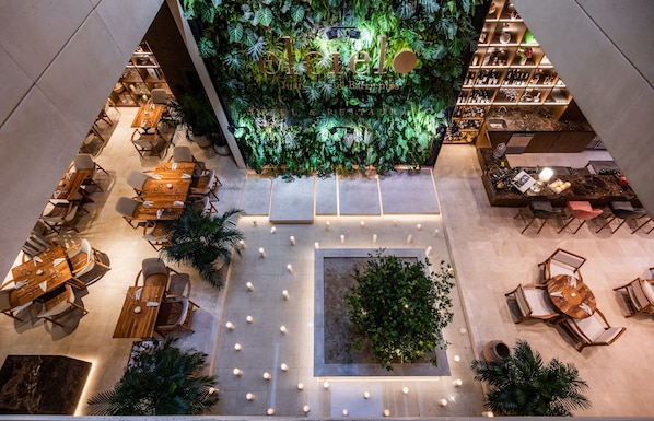 A hotel lobby with a central indoor garden, multiple seating areas, and a well-lit atrium.