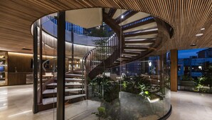 Un intérieur moderne avec un escalier en colimaçon à la rampe en verre, un plafond en bois et une vue sur le paysage urbain.