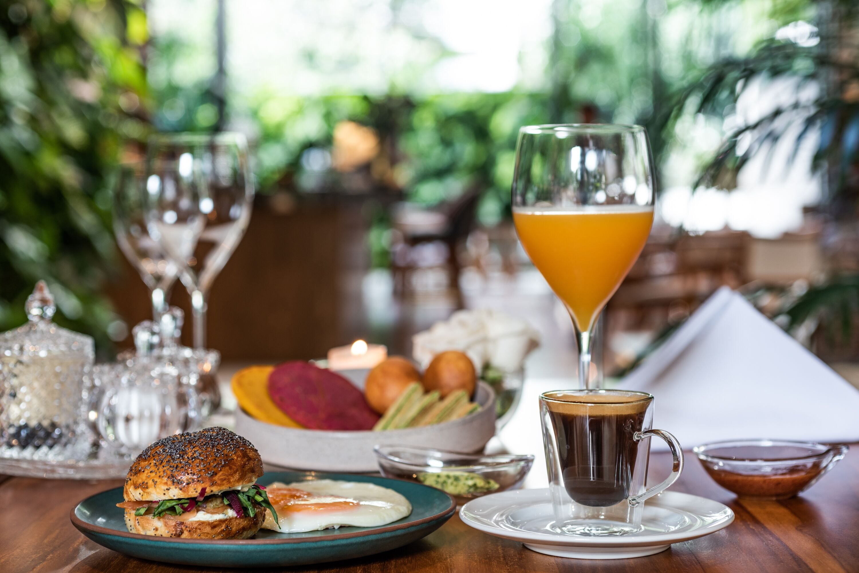 A breakfast setting with a sandwich, fruit bowl, coffee, and a glass of orange juice on a wooden table.
