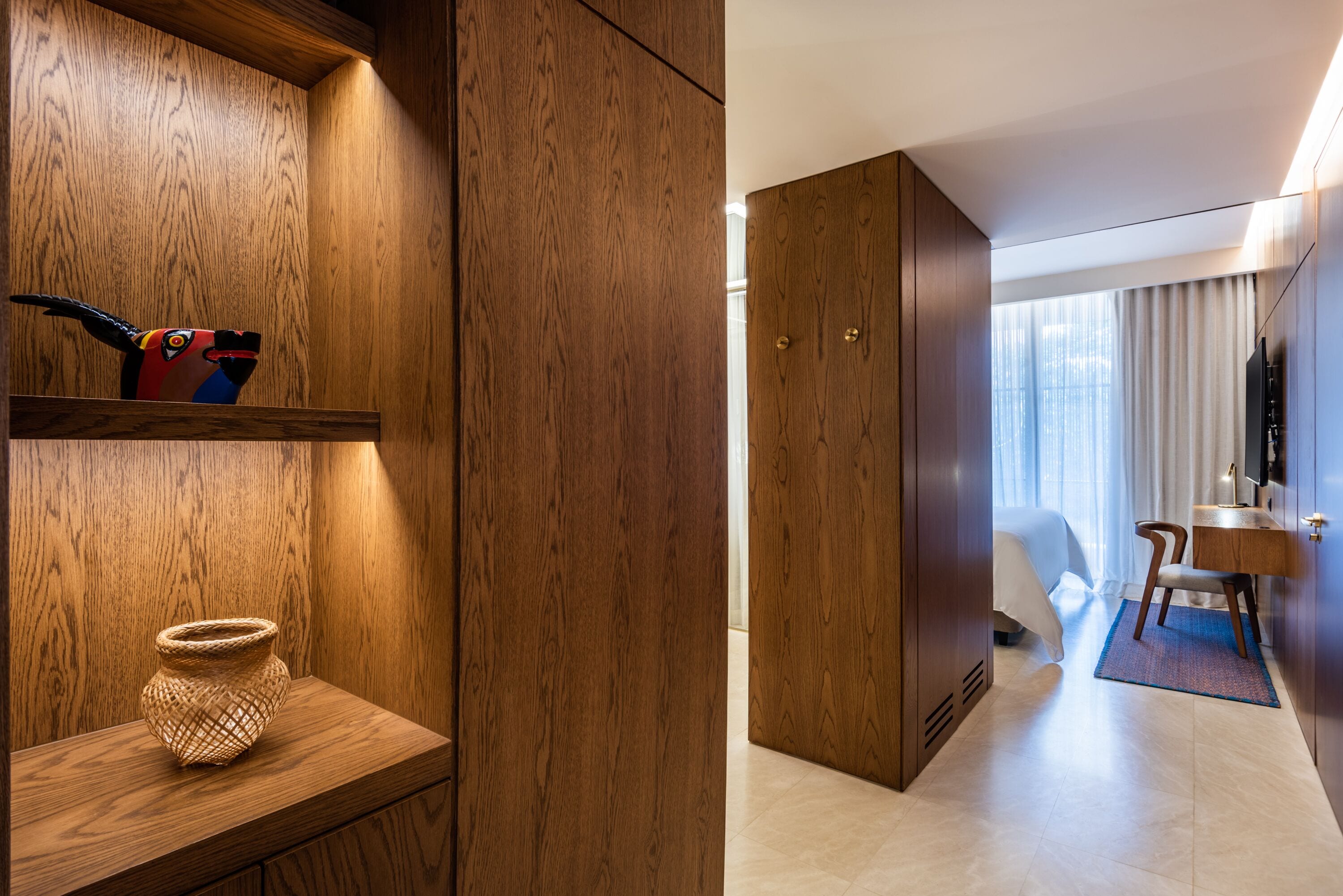 A hotel room with wooden paneling, a bed, a desk, and a television.