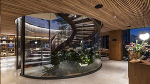 Un intérieur moderne avec un mur incurvé en verre, un escalier en colimaçon et un comptoir d’accueil agrémenté de plantes.