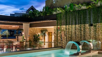 Un moderno vestíbulo de hotel con piscina, plantas de interior y una pared de piedra decorada con estrellas.