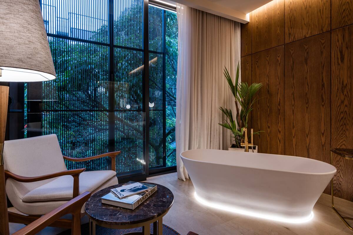 Une salle de bain moderne avec une baignoire sur pieds, un mur recouvert de panneaux en bois et une grande fenêtre donnant sur un paysage verdoyant.