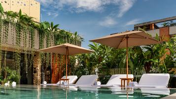 A pool area with lounge chairs and umbrellas, surrounded by lush greenery and a building with star decorations.
