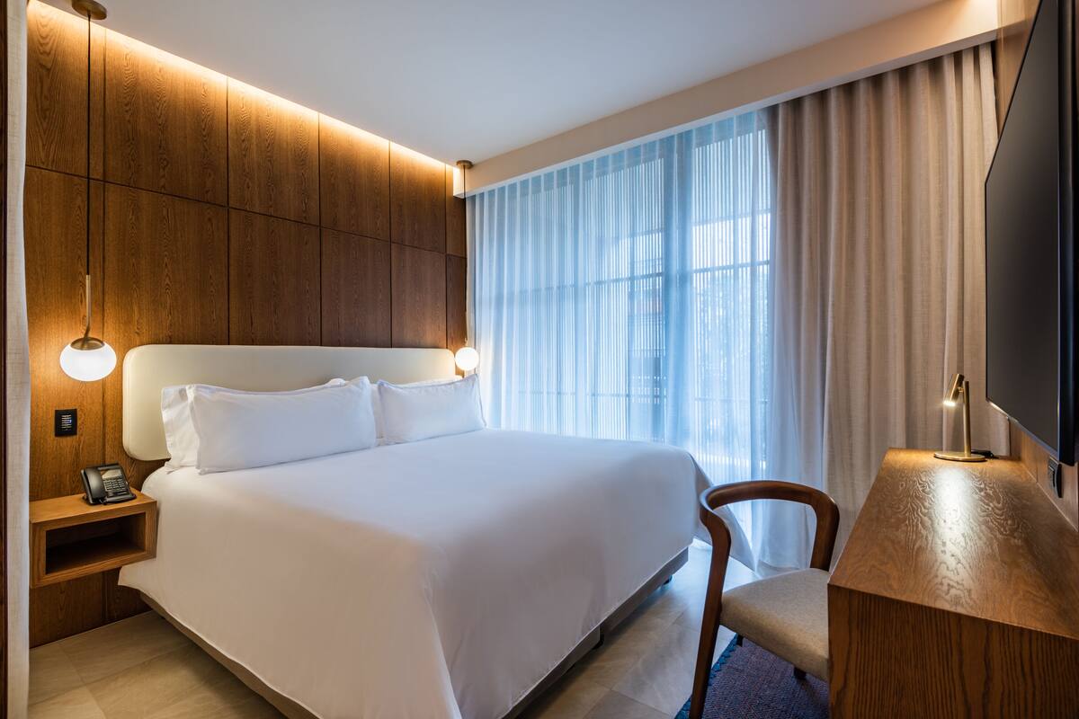 Une chambre d’hôtel avec un grand lit, une tête de lit en bois, des lampes de chevet, un bureau et une télévision.