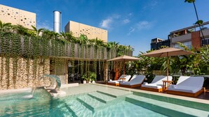 Un espace piscine agrémenté de chaises longues et de parasols, entouré de verdure et d’un mur en pierre.