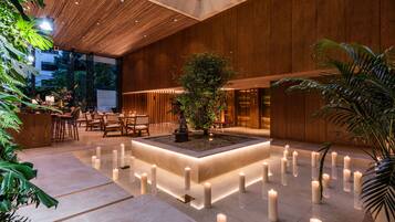 A spacious indoor area with a central water feature surrounded by candles, wooden paneling, and seating arrangements.