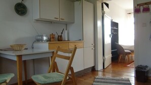 A compact kitchen with wooden chairs, a white table, and a striped rug. - Ferienwohnung A3 - One Bedroom Apartment, Sleeps 3 (Klocksin)