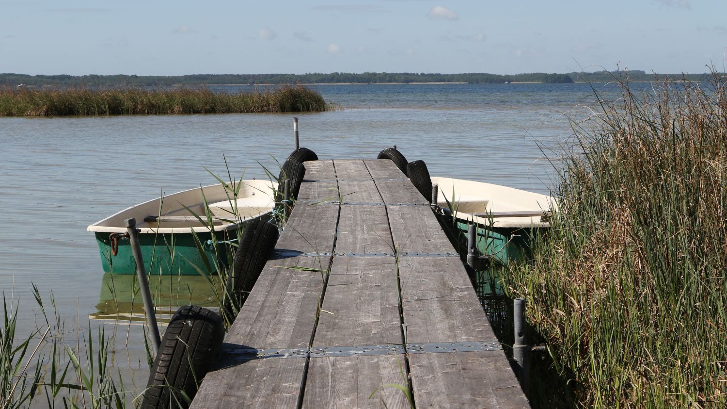 A wooden dock extending into calm water with two boats moored at the end.