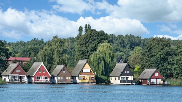 A row of traditional wooden houses with steep roofs, situated on stilts over a body of water, with a forested hill in the background. - Ferienwohnung A3 - One Bedroom Apartment, Sleeps 3 (Klocksin)
