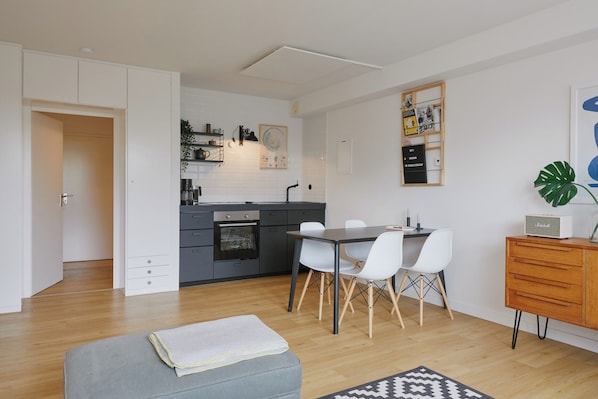 A modern kitchen with white cabinets, a dining area with a table and chairs, a gray sofa, and a wooden cabinet with a radio.