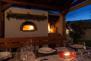 Enjoy a meal in our outdoor dining area, featuring a brick oven and a cozy table setting.