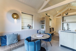 A modern living room with a sofa, blue chairs, a round table, and a kitchen area with a sink and cabinets.