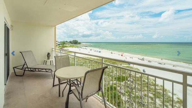 A balcony with a table and chairs, overlooking a beach with people and umbrellas.