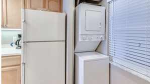 A compact kitchen with a refrigerator, a washing machine, and a window with blinds.