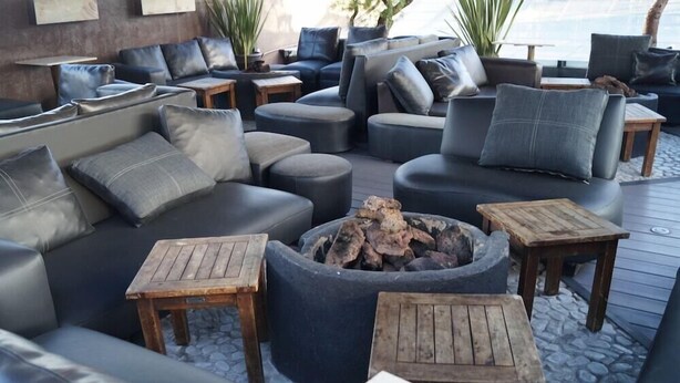 Un espace extérieur moderne aménagé avec des canapés et des tables, un foyer et des plantes en pot.