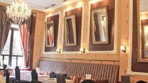 Un espace repas avec des banquettes à rayures, des lustres et des miroirs encadrés accrochés aux murs.