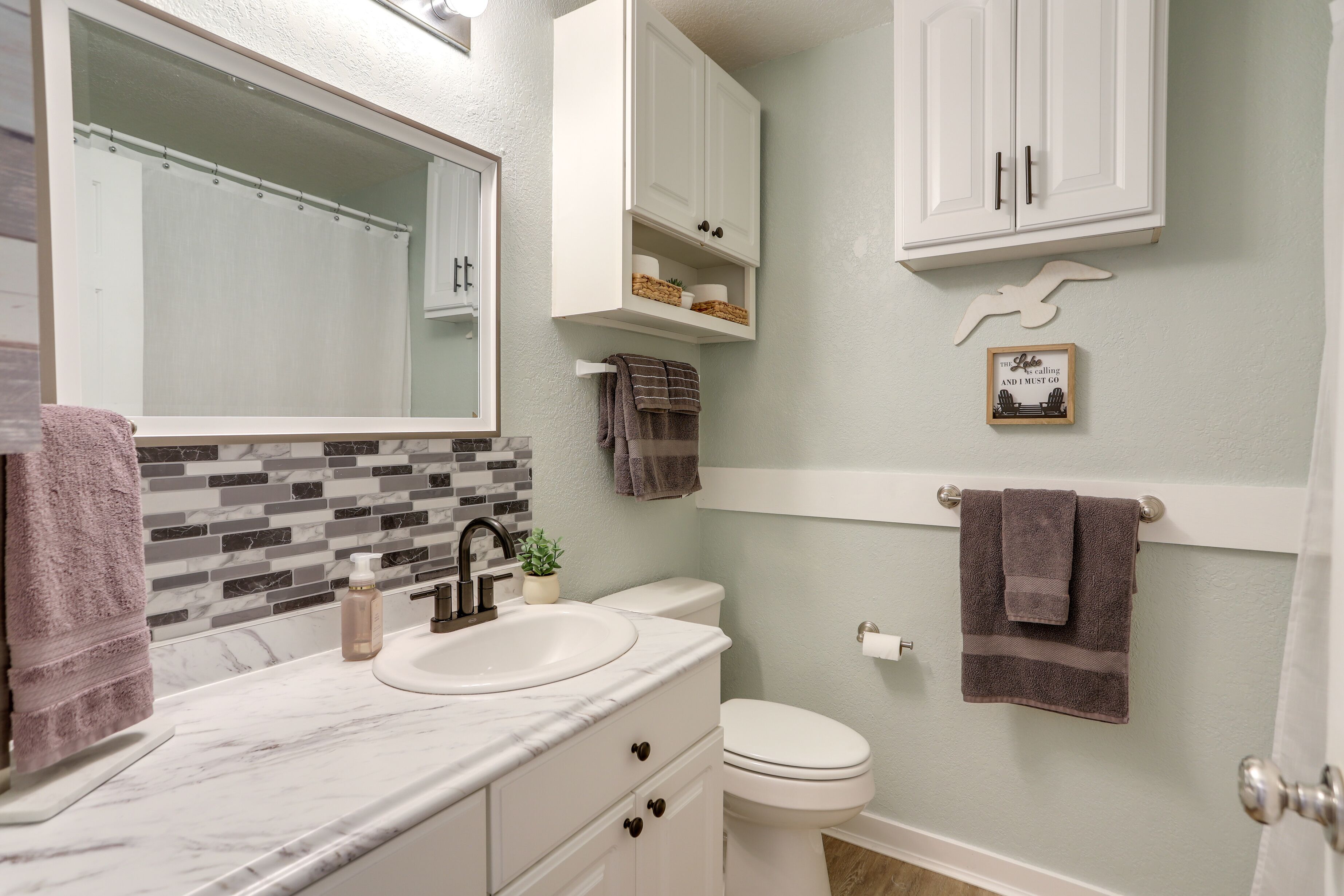 A bathroom with a white sink, a mirror, a toilet, and a cabinet above the toilet.