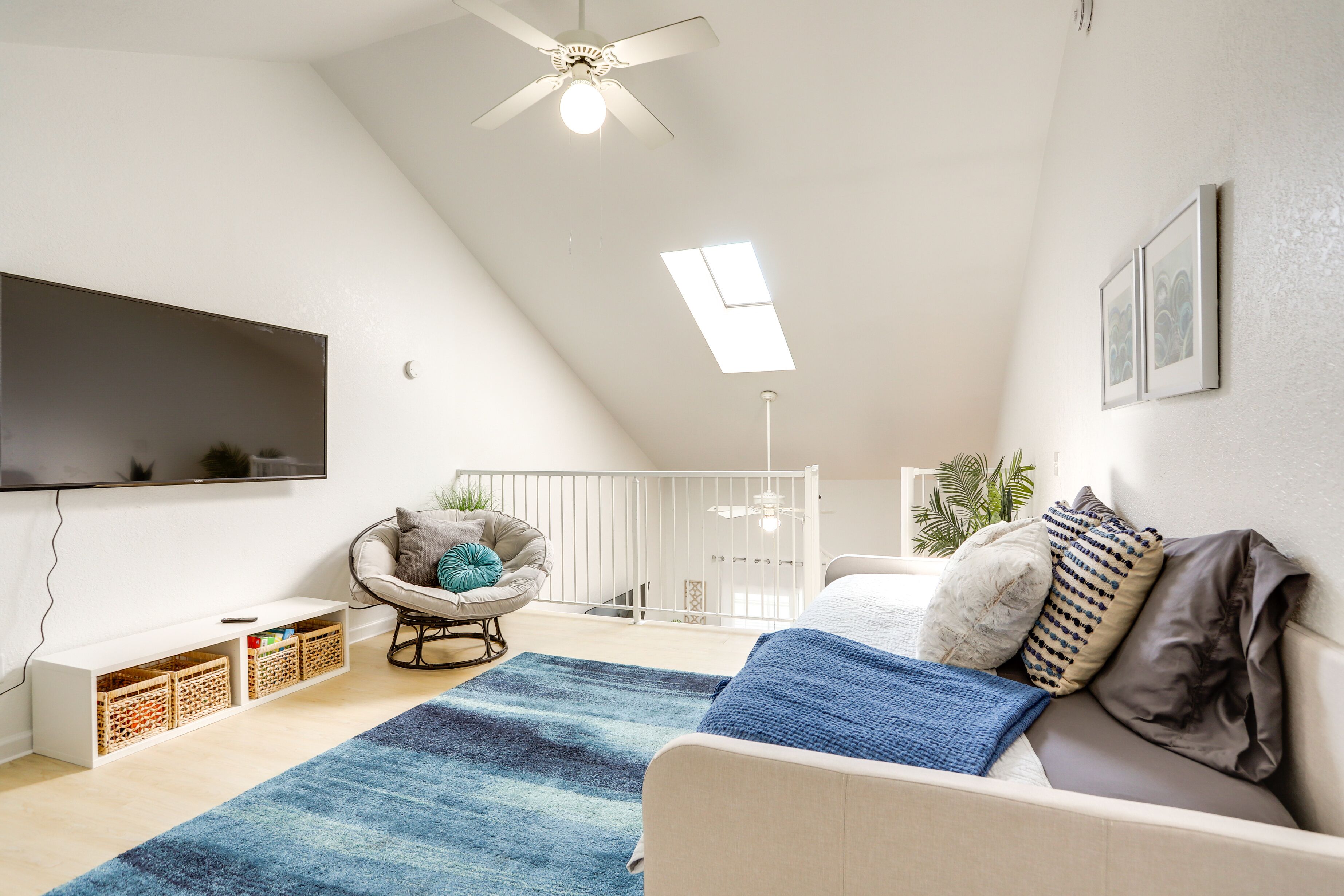 Un salon moderne doté d’un ventilateur de plafond, d’un téléviseur à écran plat, d’un canapé, d’un fauteuil et d’une petite table avec des bacs de rangement.