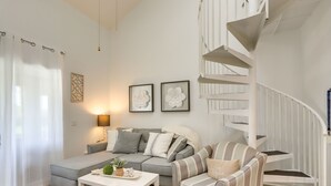 Ein modernes Wohnzimmer mit einem grauen Sofa, einem gestreiften Sessel, einem weißen Couchtisch und einer Wendeltreppe.