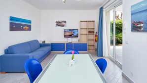 A modern living room with a sofa, a dining table with a vase, and a TV on a stand. - Scirocco, Holiday Home with garden and terrace ,100 mt from the sandy beach (Marina di Ragusa)